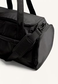 Zwarte duffelbag gemaakt van duurzaam fabric, met een ritsvak, verstelbare riem en twee stevige handvatten voor veelzijdige draagopties.