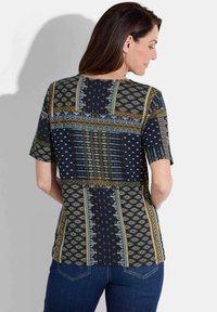 Patroon korte mouwen top met een donkerblauwe basis en gouden en blauwe geometrische ontwerpen. Zachte stof met een losse pasvorm.