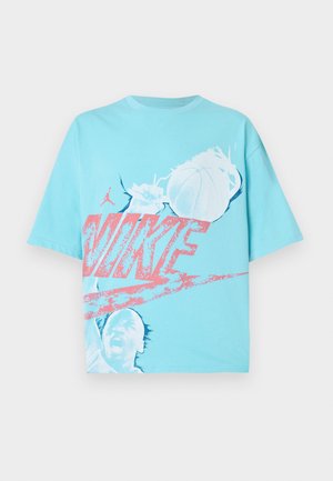 T-shirt de algodão azul claro com um proeminente logótipo rosa "NIKE", um gráfico de basquetebol e a silhueta de um jogador. Manga curta, corte descontraído.