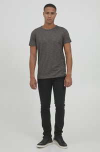 Camiseta corta de manga corta en gris oscuro con cuello redondo, combinada con jeans skinny negros y zapatillas negras con suelas blancas.