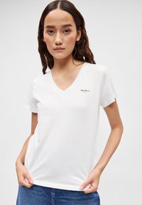 Λευκό T-shirt με V-λαιμόκοψη από βαμβακερό ύφασμα, με κοντά μανίκια και μικρό μαύρο λογότυπο. Το πουκάμισο έχει άνετη εφαρμογή και λεία υφή.