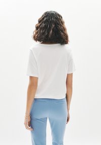 Camiseta blanca de manga corta, con cuello redondo, combinada con pantalones ajustados de color azul claro, mostrando la parte trasera y una textura lisa y sencilla.