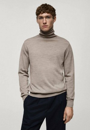 Pulover turtleneck de culoare maronie deschis, realizat dintr-un material moale; are o croială ajustată, manșete și tiv cu nervuri, asortat cu pantaloni închis la culoare.