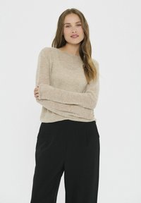 Ljus beige, mjuk stickad tröja med vid halsringning och långa ärmar, kombinerad med svarta, skräddarsydda byxor. Slät textur och avslappnad passform.