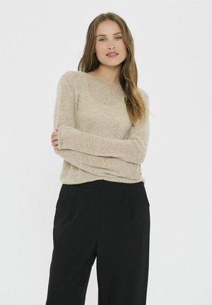 Hellbeige, weicher Strickpullover mit weitem Ausschnitt und langen Ärmeln, kombiniert mit schwarzen, maßgeschneiderten Hosen. Glatte Textur und lockere Passform.