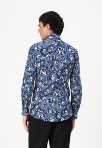 Camicia a maniche lunghe di colore blu con motivo floreale bianco, crema e blu navy. Presenta un colletto e chiusura con bottoni, realizzata in un tessuto liscio.