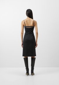 Sort satin slip-kjole med tynde stropper, knælang, med et rektangulært udskæring bagpå. Båret sammen med knæhøje sorte høje støvler.