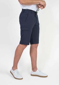 Marine cargo shorts met een trekkoord in de taille, zijzak en een rechte snit. De stof lijkt glad en heeft een lichtgewicht textuur. Draagt met witte sneakers.