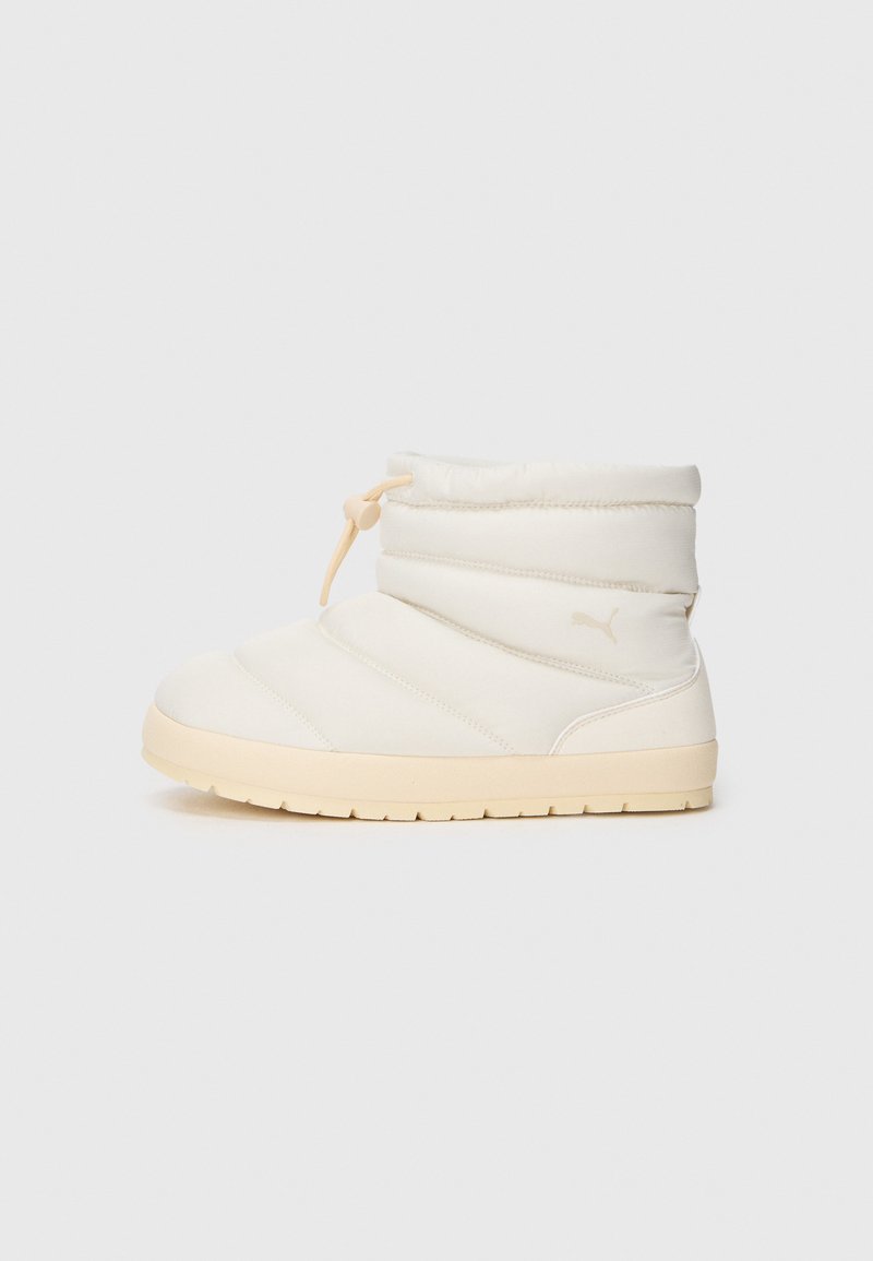 Kremfargede polstrede ankelstøvler med beige såle og justerbar snorlukking på en ensfarget hvit bakgrunn.