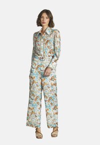 Combinaison à motif floral avec un col, des manches longues, une taille ceinturée et des jambes larges dans des nuances de bleu et de marron.