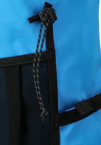 Corda di chiusura bianca e nera con fermo in plastica su tessuto blu e nero, parte di uno zaino o borsa impermeabile.