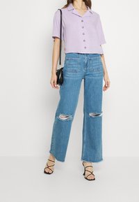 Lavendelfärgad kortärmad skjorta med krage, kombinerad med ljusblå vida jeans med trasiga knän och två bakfickor.