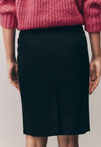Svart pennkjol i ett slätt tyg, knälång med en bakre slits. Sammanställd med en rosa stickad tröja som visar ett strukturerat stickat mönster.