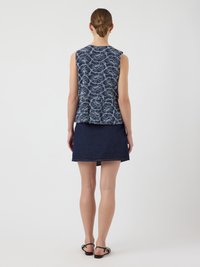 Haut sans manches bleu marine avec un léger motif floral, design peplum. Associé à une jupe en denim foncé, longueur cheville, et des sandales noires.