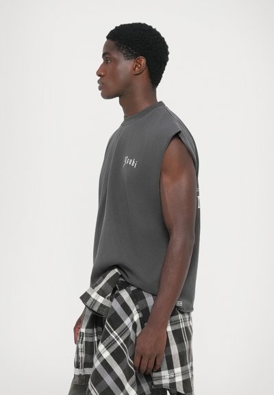 Houtskoolkleurige mouwloze sweatshirt met een ronde halslijn, voorzien van een witte logo-detail. Gestyled met een zwart-wit geruite overhemd knoop in de taille.