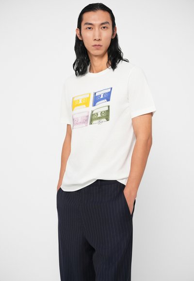 Balta medvilninė marškinėliai su keturių spalvotų kasetinių juostų grafika: geltona, mėlyna, rožinė ir žalia. Apvalus kaklas ir trumpomis rankovėmis.