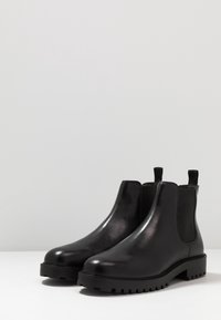 Botas Chelsea de cuero negro con un acabado suave, paneles laterales elásticos y una suela de goma resistente que presenta un patrón de dibujo pronunciado.