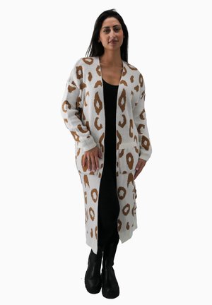 Langer Strickcardigan in Creme mit braunem Leopardenmuster, mit langen Ärmeln, offener Front und Taschen. Kombiniert mit einem schwarzen Kleid und Stiefeln.