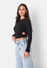 Svart ribbad långärmad crop top med sidoutsparningar och snörningar, kombinerad med ljusblå högmidjade baggy jeans.