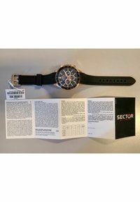 Orologio con cinturino in gomma nera e dettagli in oro, quadrante rotondo nero, tre sub-quadranti cronografici e logo del marchio visibile. Include dettagli sulla garanzia.