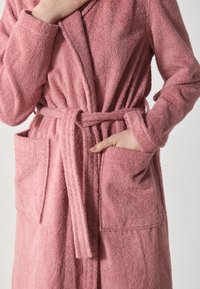 Rosa frotté badekåpe med lange ermer, belte, og to frontlommer; myk tekstur og enkelt design.