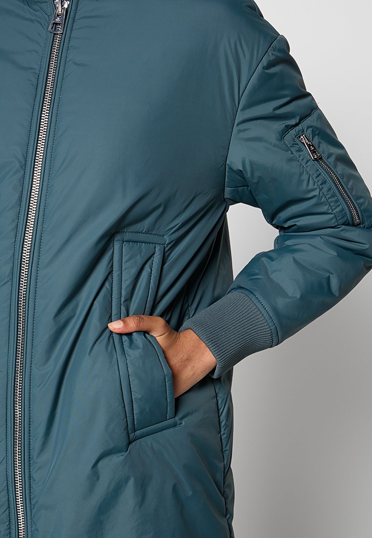  Gepolsterte türkise Jacke mit silbernem Reißverschluss, gerippten Bündchen und einer Seitentasche. Sie zeichnet sich durch ein elegantes Design mit glatter Textur und praktischen Details aus.