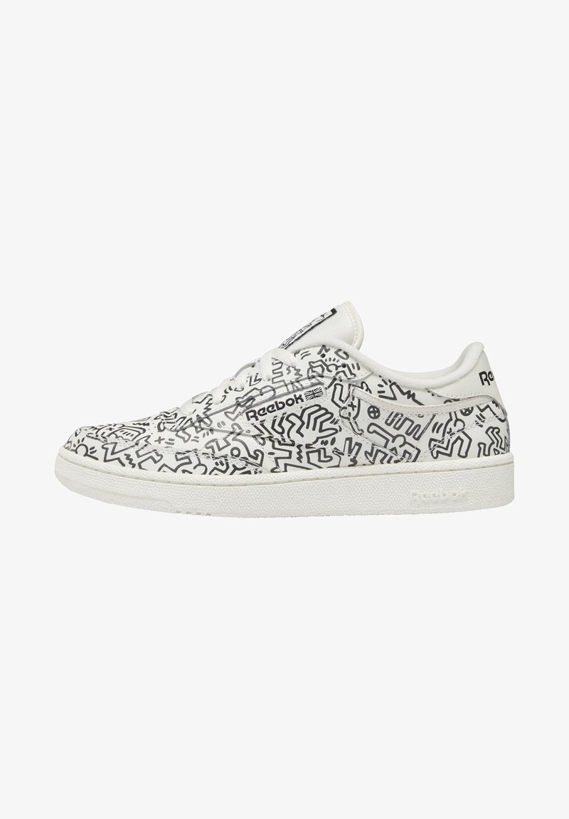 Baskets blanches avec motifs abstraits noirs en lignes, dotées d'un design à lacets, d'un bout arrondi et d'une semelle en caoutchouc texturée. Marque Reebok visible.