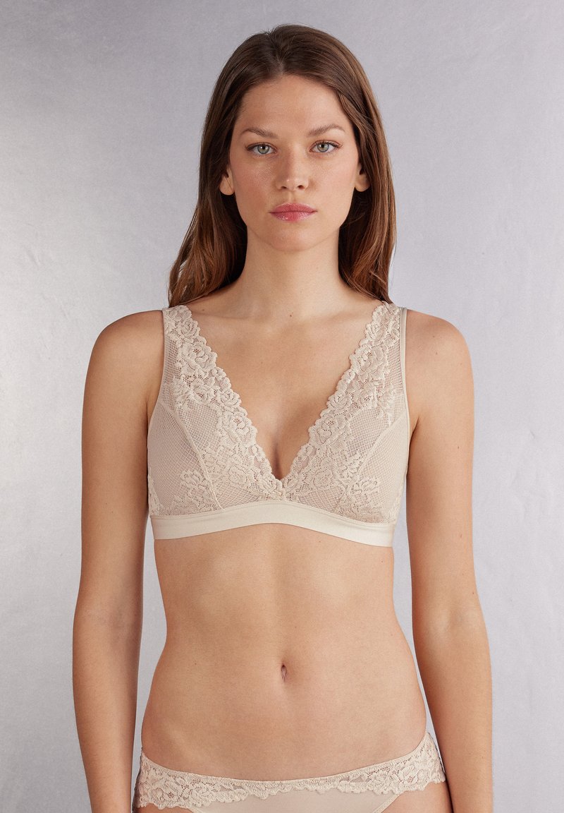 Beige spets-bra med djup V-hals, bred spetskant och mjuk, stretchig underband. Slät yta med intrikata blommönster.