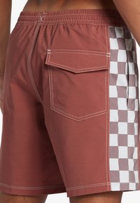 Men's swim shorts in rust color with white stitching. Features a back pocket and side checkered pattern in light brown and white.