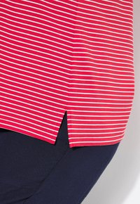 Haut rayé rouge et blanc avec une fente sur le côté, fabriqué en tissu doux, associé à un pantalon bleu marine. Gros plan sur l'ourlet et la texture.