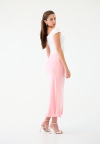 Top bianco aderente con maniche corte, abbinato a una gonna in satin rosa pallido con uno spacco laterale e bottoni, completato da tacchi beige con cinturini.
