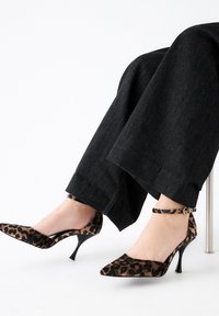 Tacones de leopardo de punta afilada, con tacón de aguja negro y tira en el tobillo. La suave textura del tejido complementa el audaz estampado.