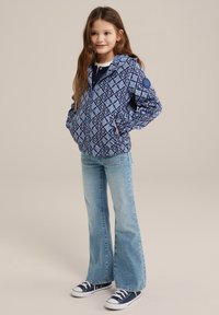 Blå mönstrad zip-up hoodie med geometrisk design, huva och fickor, matchad med ljus tvättade utsvängda jeans och marinblå sneakers.