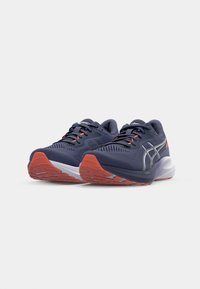 Baskets de sport bleu foncé avec des accents argentés, tige en maille texturée et semelle en caoutchouc orange. Comprend une semelle intermédiaire rembourrée pour le soutien.