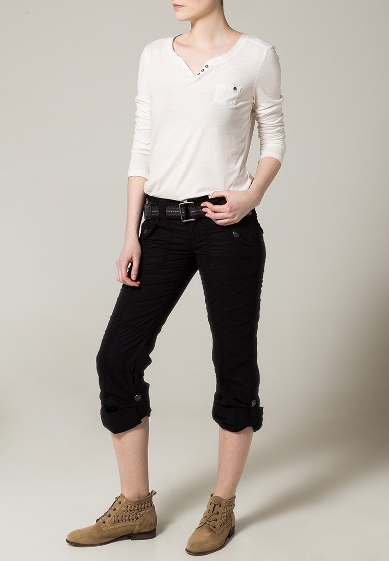 Chemise longue à manches longues beige clair, pantalon noir raccourci avec poignets retroussés et bottines tan à lacets avec un point de décoration.