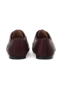 Burgunderfarbene Slipper mit einer strukturierten, haarähnlichen Oberfläche, runder Zehenpartie und schwarzer flacher Sohle. Minimalistisches Design, ohne sichtbare Beschläge.