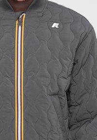 Γκρι τζάκετ με επένδυση, με ριγέ γιακά, διαθέτοντας μπροστινό φερμουάρ με πολύχρωμες ρίγες και λογότ�υπο στην αριστερή πλευρά.