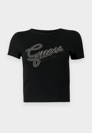 Juoda trumpomis rankovėmis prigludusi marškinėliai iš struktūrinės medžiagos, su „Guess“ logotipu ir „EST. 1981“ užrašu, puoštomis cirkoniais ir rašytiniu šriftu.