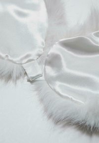 Mascherina da notte in raso bianco rifinita con morbido finto pelo. Include un cinturino in tessuto per una migliore aderenza. Texture liscia con soffici dettagli in pelliccia in rilievo.