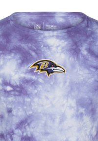 Lila tie-dye t-shirt med en Baltimore Ravens-logotyp i gult och svart på bröstet, tillverkad av mjukt tyg med rundad halsringning.