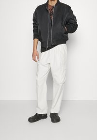 Black bomber jacket, white cargo pants, and black clogs. The jacket has a zip front, ribbed cuffs, and a small logo. Pants feature side pockets.