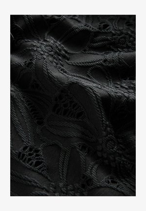 Tissu noir présentant des motifs floraux en dentelle complexe avec une texture en relief et des détails coupés, créant une apparence superposée et dimensionnelle.