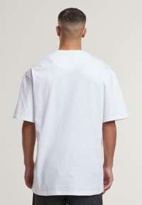 White cotton T-shirt with short sleeves, a relaxed fit, and a plain design. The back features a rounded neckline and no visible logos or patterns.
