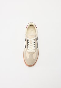 Sneaker mit einem Obermaterial aus beigem und grauem Wildleder, schwarzen seitlichen Streifen, weißen Schnürsenkeln und einer braunen Gummisohle, ergänzt durch einen bordeauxroten Fersenakzent.