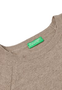 Beżowy sweter z dzianiny z dekoltem i ściągaczem, w kolorze zielonym metka z napisem "United Colors of Benetton" wszyta wewnątrz kołnierza.