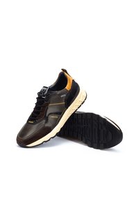 Zapatillas con un upper de cuero y ante marrón oscuro, acentos amarillos y una suela de goma negra texturizada que presenta un patrón geométrico.