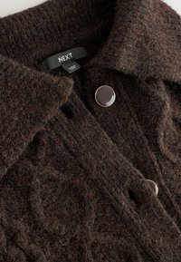Brauner gestrickter Cardigan mit einem strukturierten Muster, dunklen Knöpfen und einem Kragen. Das Etikett trägt die Aufschrift "NEXT". Weiches, dickes Material mit einem gemütlichen Aussehen.