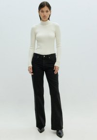 Geribbeld, hoog col, langemouwen top in off-white, gecombineerd met zwarte flared jeans. Schoenen zijn zwarte puntige hakken. Eenvoudig, aansluitend ontwerp.