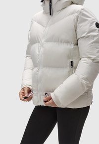 Giacca a vento bianca con zip frontale, cuciture a zig-zag, polsini elasticizzati e due tasche laterali con zip, con dettagli in metallo nero.