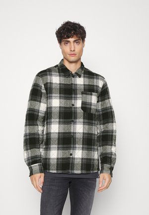 Black and white plaid flannel shirt with a buttoned collar and single chest pocket, featuring a textured fabric design.
